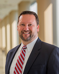 Photograph of Steven Kailes in a black suit and red tie